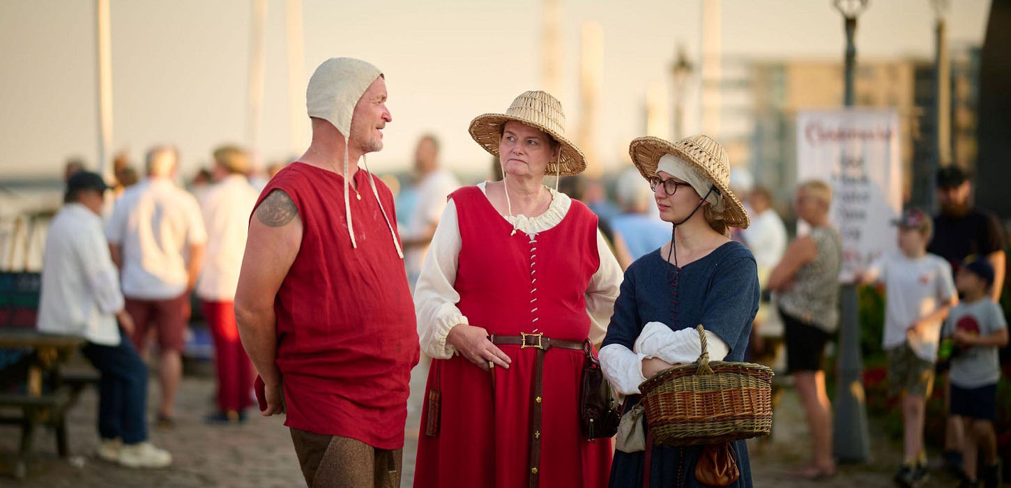 Tre middelalderpersoner står på marinaen under Danehof